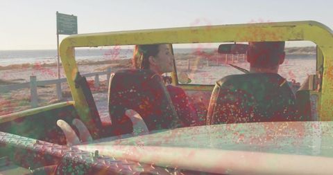 Couple chatting in yellow off-road vehicle on coastal road with surfboard and sunset ocean