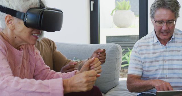 An elderly woman wears a VR headset and experiences virtual reality, supported by friends in a modern living room. Ideal for topics related to senior engagement with technology, intergenerational bonding, and elder care innovation.