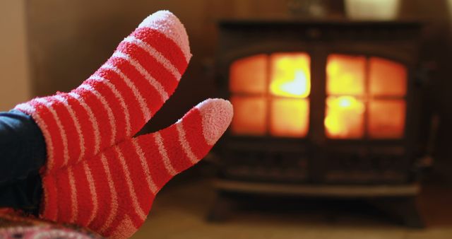 Feet in cozy striped socks are warming up in front of a glowing fireplace, with copy space. It's a comforting scene that evokes the warmth and relaxation of a cold day spent indoors.