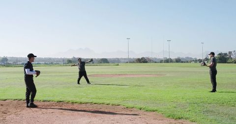 Three men practicing baseball throwing on sunny outfield with mountain backdrop