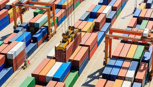 Gantry crane lifting cargo container over busy port terminal with stacked multicolor boxes