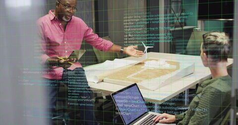 Senior architect presenting scale model with coding overlay while team reviews design