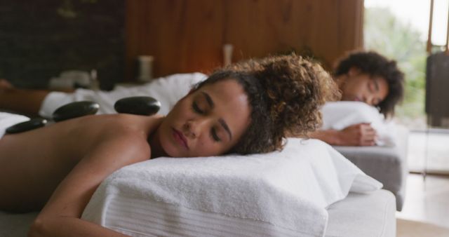Couple lying on spa beds while receiving relaxing stone massage therapy. Ideal for uses related to wellness, relaxation, spa treatments, luxury pampering services, and self-care.