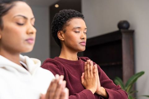 Indian and african american women meditating with hands in prayer for mindfulness and calm