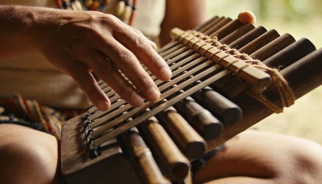 Playing handcrafted bamboo instrument on lap in garden with beaded necklace