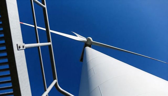 Rising wind turbine tower capturing low-angle nacelle and blades against clear blue sky