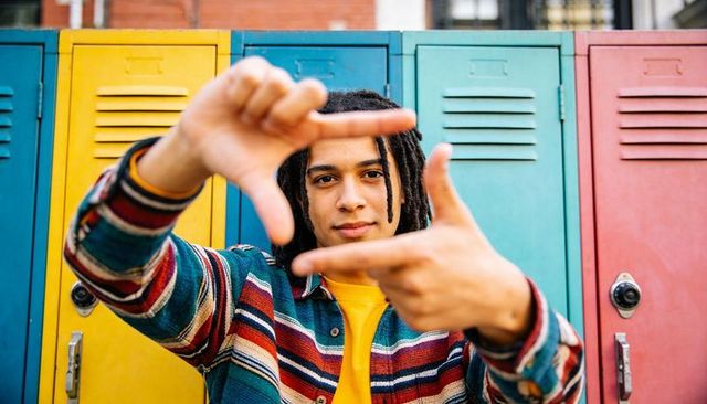 Student framing hands in front of colorful school lockers, dreadlocks, striped flannel