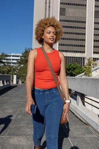 Confident african american woman walking urban walkway wearing red tank top and jeans