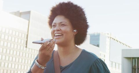 Happy Biracial Woman Using Smartphone with Earphones Outdoors