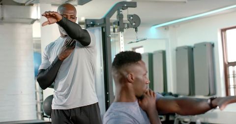 African american trainer guiding client stretching wearing compression sleeves in gym