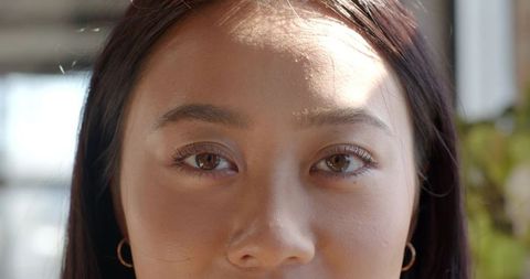 Asian Woman with Radiant Skin and Gold Hoop Earrings in Bright Room