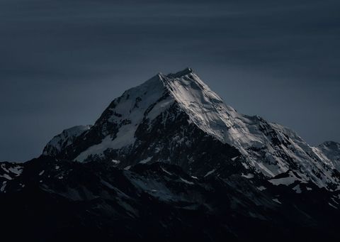 Snow-Capped Peak Towering Over Dark Alpine Ridge at Dusk with Moody Twilight Light