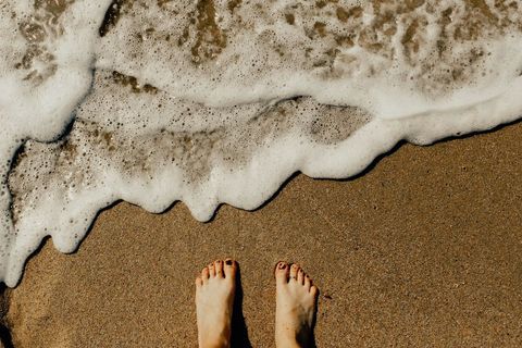 Standing barefoot on sandy beach with incoming foamy wave