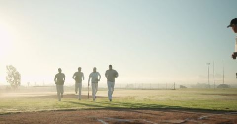 Morning baseball team jogging across sunlit diamond during warmup holding wooden bat