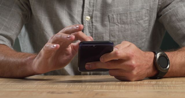 Close-up view of person using smartphone. Wearing grey shirt and smartwatch. Suitable for illustrating concepts of technology, online communication, and modern lifestyle. Ideal for blogs, online articles, and promotional materials relating to digital communication or smart devices.