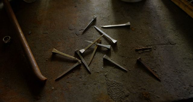 A collection of metal nails scattered on a worn, dark workbench. Ideal for illustrating themes of manual labor, craftsmanship, or industrial settings. Suitable for use in blog posts, articles about DIY projects, industrial and mechanical work, or educational materials about tools and machinery.