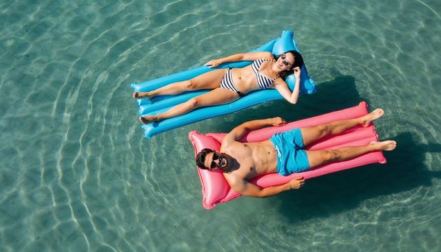 Summer couple floating on inflatable loungers in crystal-clear shallow water