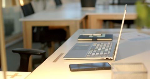 Slim silver laptop resting on white desk in minimalist workspace with phone and notebook