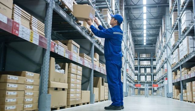 Warehouse worker reaching for carton on high rack in modern fulfillment center