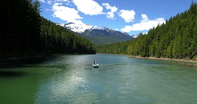 This serene scene captures a person canoeing on a tranquil lake surrounded by dense pine forests and under a clear blue sky with mountain peaks in the background. Ideal for use in travel brochures, outdoor adventure promotions, nature conservation campaigns, or as a powerful visual for relaxation and meditation content.
