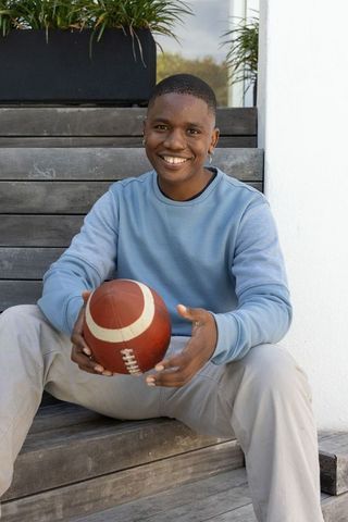 Smiling african american young man sitting on steps holding football casual lifestyle