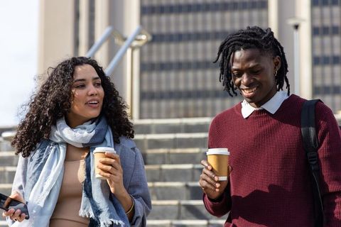 Diverse young professionals walking with coffee on city office steps, casual conversation
