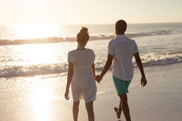 Couple enjoying a romantic walk on the beach during sunset, holding hands and savoring the serene moment. Perfect for use in travel brochures, relationship blogs, romantic getaway advertisements, and lifestyle magazines to convey themes of love, connection, and relaxation.