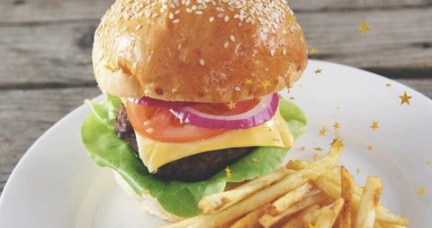 Stacking gourmet sesame cheeseburger with melted cheddar, lettuce, tomato and fries on white plate