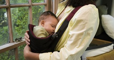 Mother holding sleeping baby in cozy carrier near window