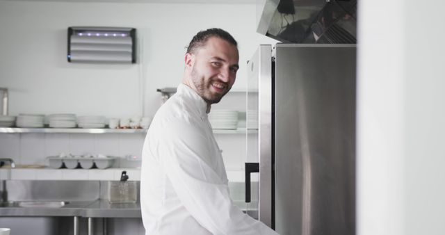 Professional chef smiling while working in a well-equipped commercial kitchen, engaging in daily tasks. Ideal for use in culinary institutes, cooking classes, advertisements for kitchen equipment or appliances, restaurant promotions, and hospitality industry marketing materials.