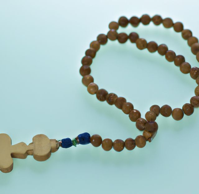 Wooden rosary beads in a loop with a cross attached, displayed on a light-colored background. The wooden beads have a blue accent near the cross. Suitable for topics related to Christianity, spirituality, prayer, and devotion. Useful for religious articles, blogs, and educational materials.
