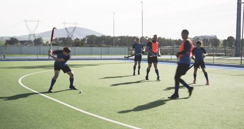 Diverse field hockey team practicing striking techniques on turf