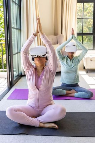 Diverse women practicing vr yoga at home wearing white headsets for mindful fitness