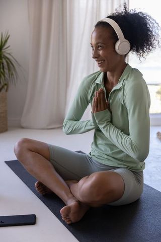 African american woman practicing yoga with headphones on home mat smiling for mindfulness