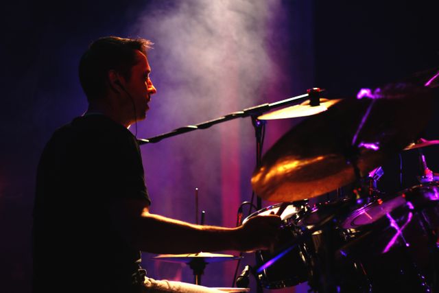 This visual captures a drummer passionately performing on stage, enveloped in atmospheric smoke and dramatic lighting effects. Ideal for use in promotional materials for music concerts, festivals, or events celebrating live performances and musical talent. Perfect for illustrating themes of rhythm, energy, and artistic expression.