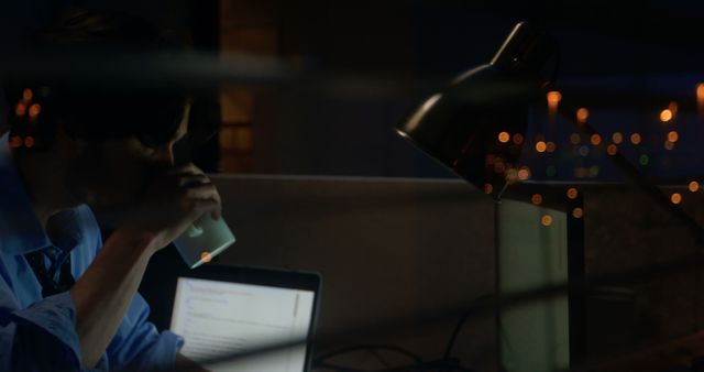 Office worker staying late hours, drinking coffee and relying on a laptop screen to finish tasks. Scene portrays dedication, focus, and productivity under minimalistic settings. Suitable for themes related to corporate lifestyle, overtime work, remote work, and work-related stress.