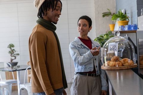 Friends choosing pastries at cafe counter with croissant dome, qr code and takeaway coffee