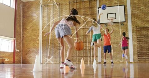 Teen girl dribbling basketball through cones in school gym practicing ball control agility