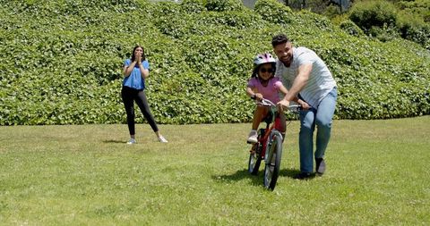 Family Teaching Daughter to Ride Bicycle on Sunny Day in Green Park