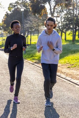 Teenage friends jogging together in sunlit park wearing smartwatches and athletic gear
