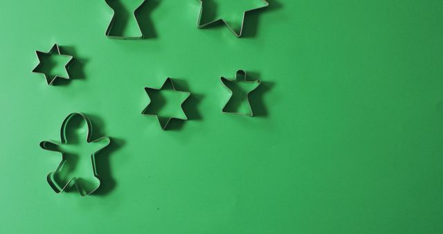 Assorted Christmas-themed cookie cutters placed on a vibrant green background. Shapes include stars, a gingerbread man, and seasonal icons. Perfect for holiday baking projects, festive decoration ideas, and illustrations for Christmas traditions or culinary articles.