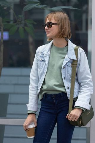 Young woman standing with coffee wearing denim jacket, sweatshirt and sunglasses