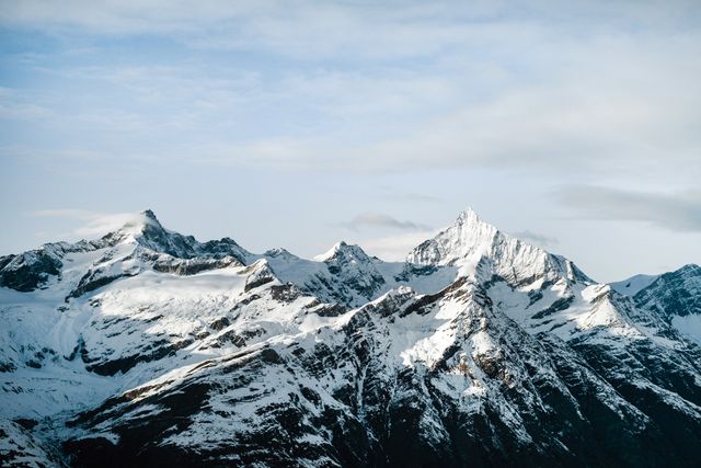 Snow-capped mountain peaks set against a clear sky with minimal clouds visible. This scenic view captures the beauty and majesty of untouched wilderness. Ideal for use in travel promotions, outdoor adventure advertisements, environmental campaigns, or as serene desktop Wallpapers.