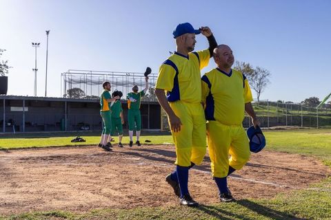 Two baseball players walking off infield in yellow uniforms holding blue caps after play