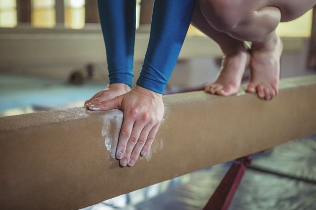 This image shows a close-up of a female gymnast's hands and feet as she practices on the balance beam. The focus on her hands gripping the beam with chalk highlights the precision and strength required in gymnastics. This image can be used for sports training materials, gymnastics promotions, or articles on athleticism and discipline.