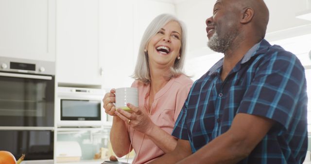 Happy mature couple smiling and enjoying morning coffee in bright, modern kitchen. Perfect for concepts related to retirement, active aging, positive senior lifestyle, love, relationships, and home living.