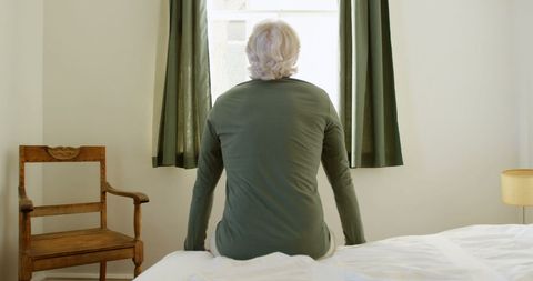Senior man reflecting while sitting on bed near window