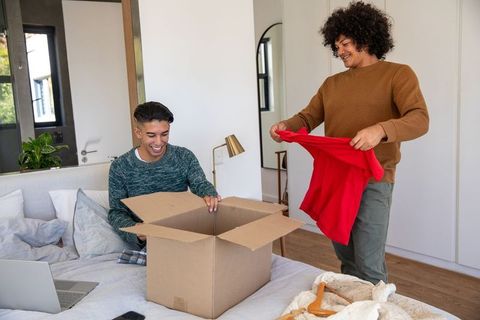 Young Friends Unpacking Box on Bed in Bright Bedroom