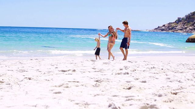 Family enjoying a sunny day at the beach, playing and holding hands near the water. Ideal for concepts related to family bonding, summer vacations, outdoor fun, and childhood memories. Perfect for travel agencies, family-oriented blogs, summer activity promotions, and beach holiday advertisements.