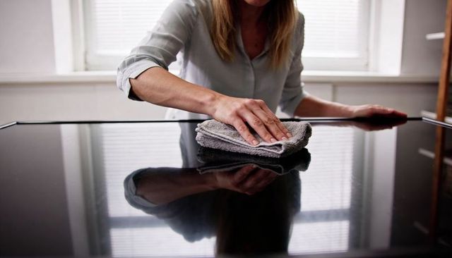 Woman wiping glossy tv screen with microfiber cloth, window reflection, home cleaning
